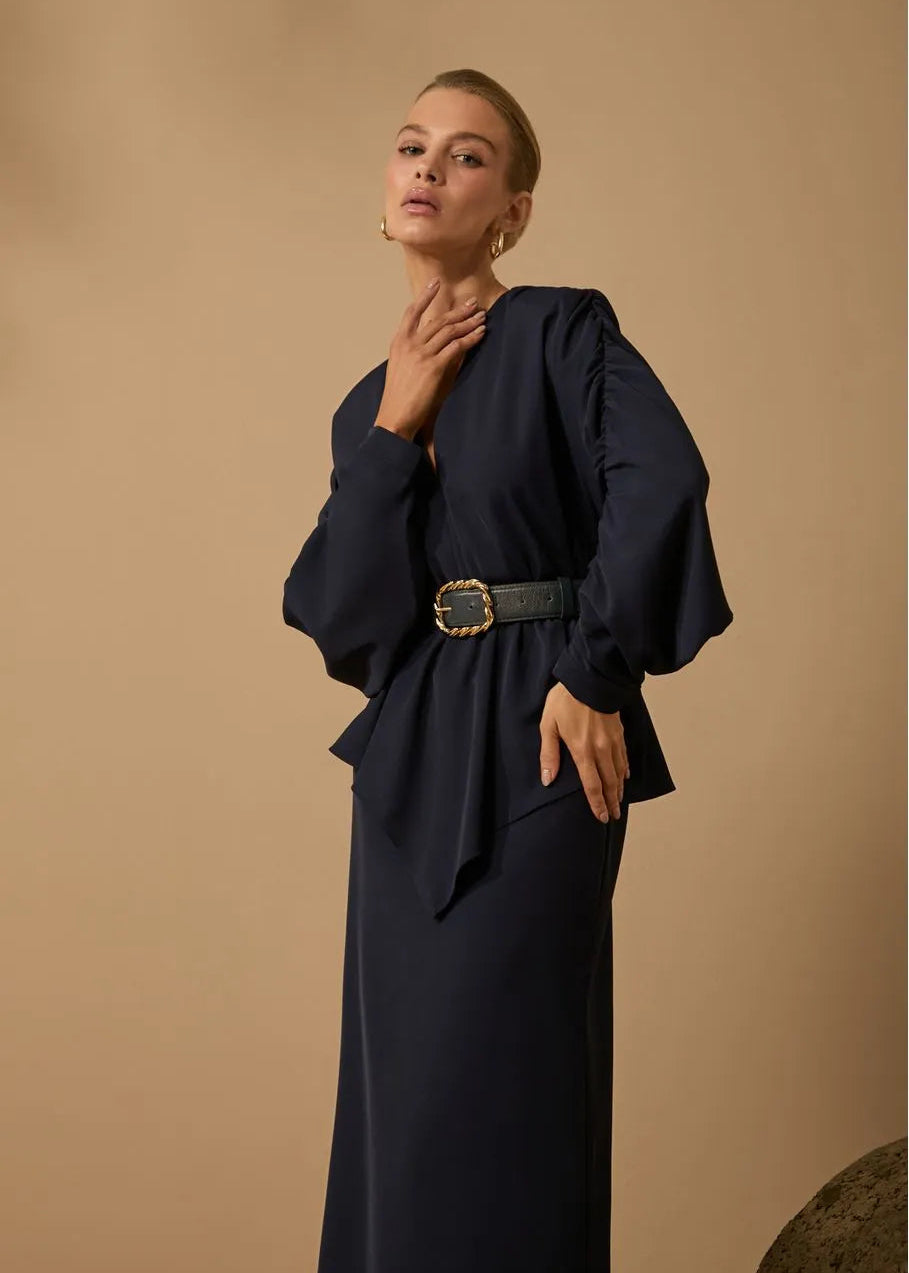 Woman wearing a dark blue dress with a belt against a beige background