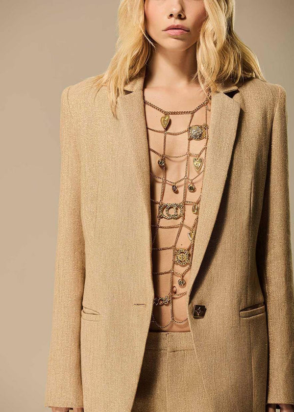 Woman wearing a beige suit with a patterned top against a neutral background