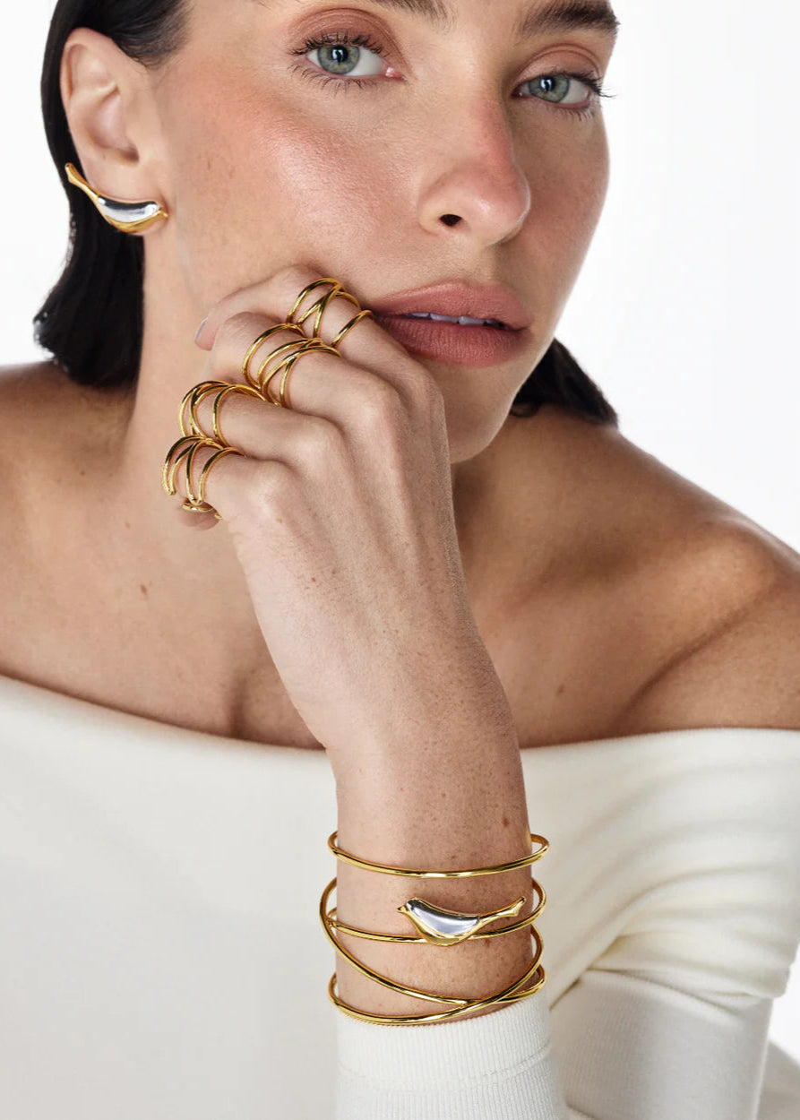 Woman wearing gold jewelry including earrings, rings, and bracelets on a white background