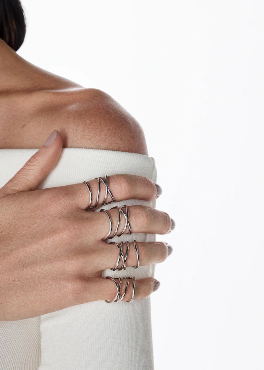 Close-up of a hand wearing multiple silver rings holding a white cup against a neutral background