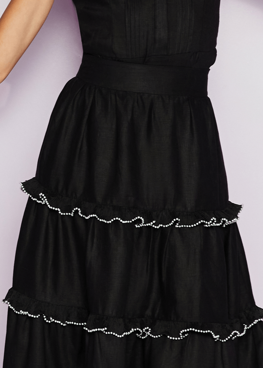 Black dress with tiered skirt and decorative hem on a light purple background