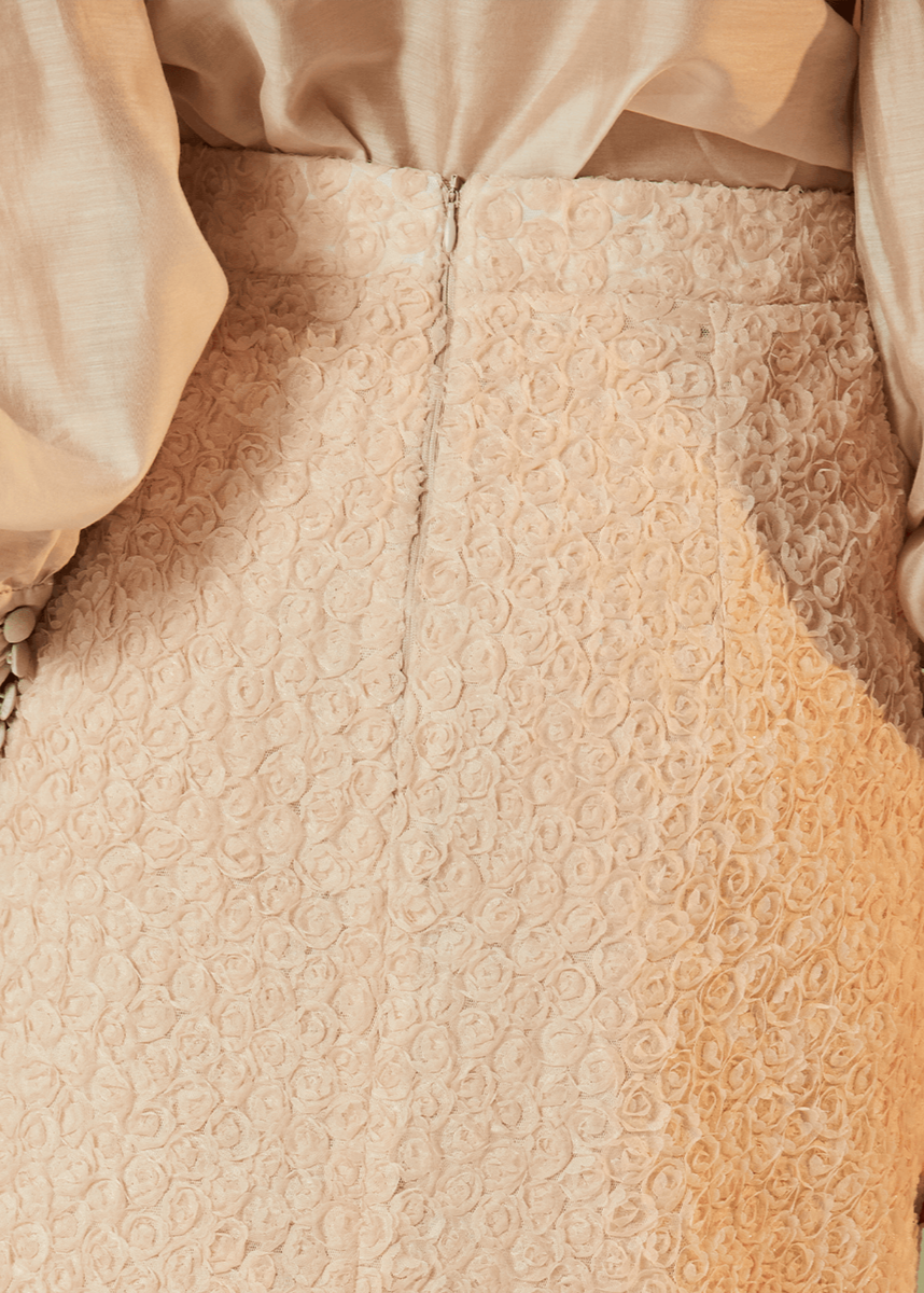 Close-up of a person wearing a beige blouse with long sleeves and a textured beige skirt.
