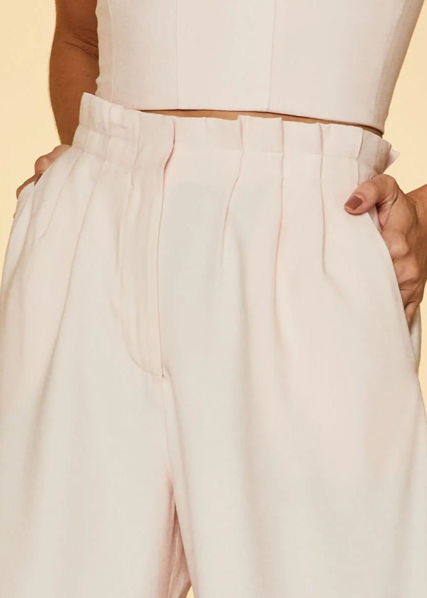 Person wearing a white sleeveless top and light pink wide-leg pants on a yellow background