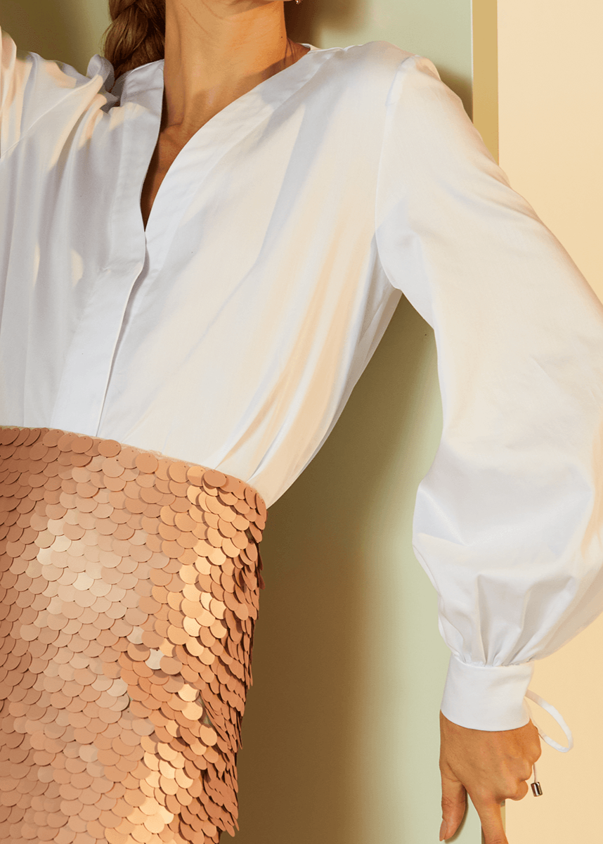Person wearing a white blouse with long sleeves and a sequined skirt.