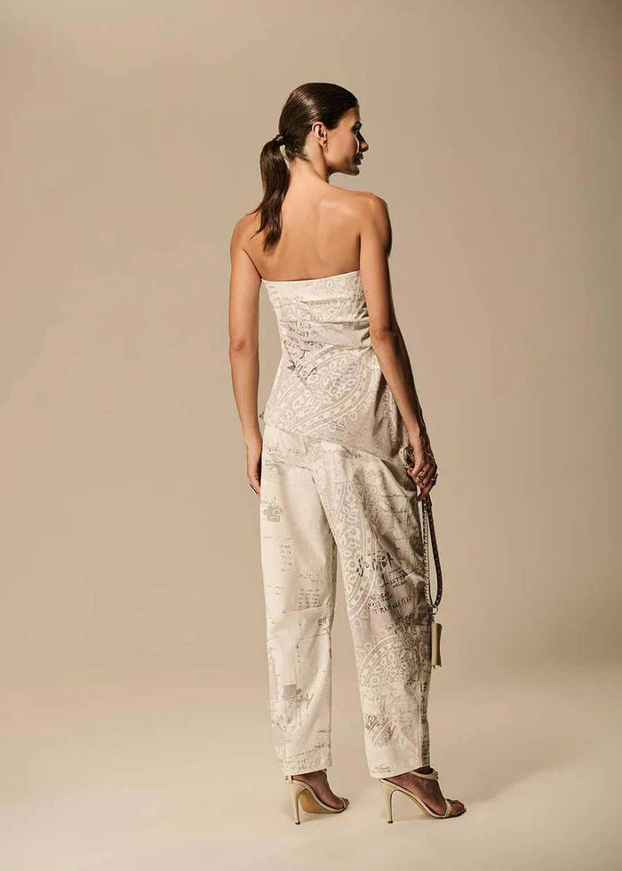 Woman wearing a strapless embroidered jumpsuit on a beige background