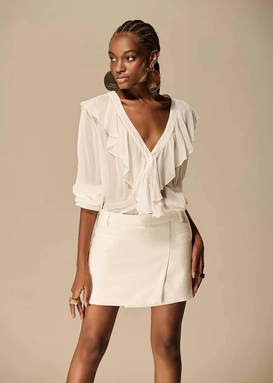 Woman wearing a white blouse and skirt against a beige background