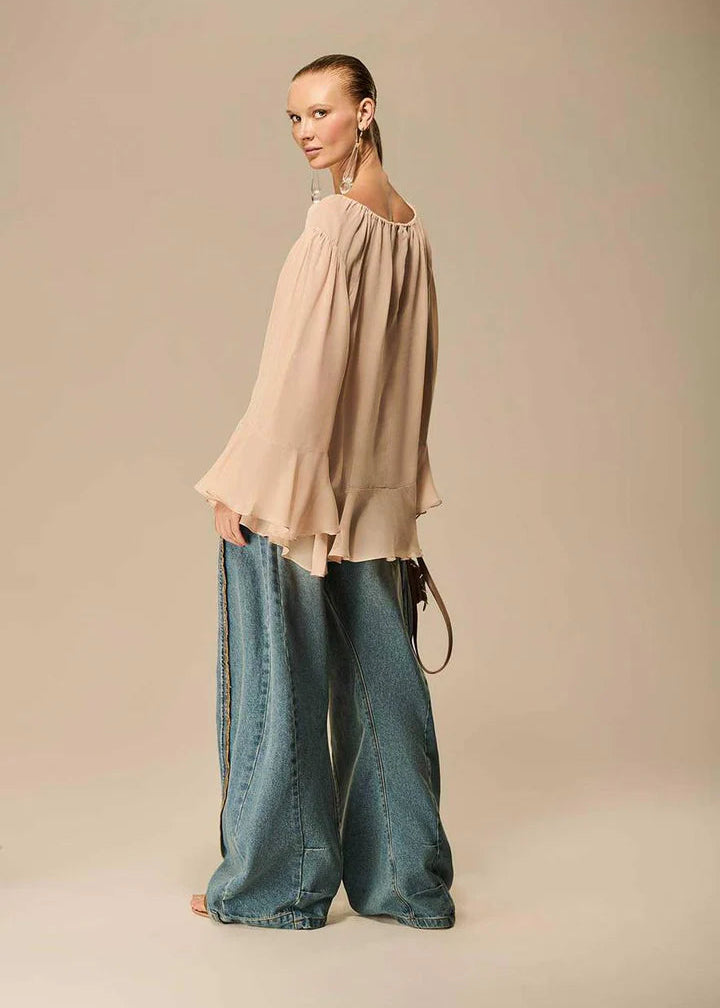 Woman wearing a beige blouse and blue jeans on a beige background