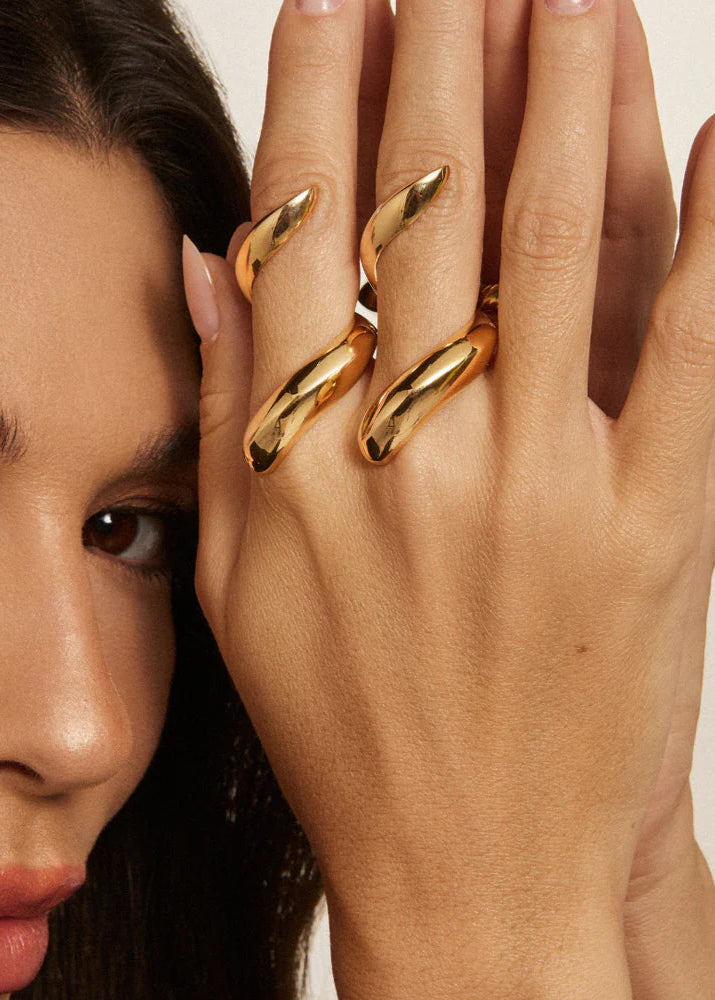 Woman wearing two gold rings on a neutral background