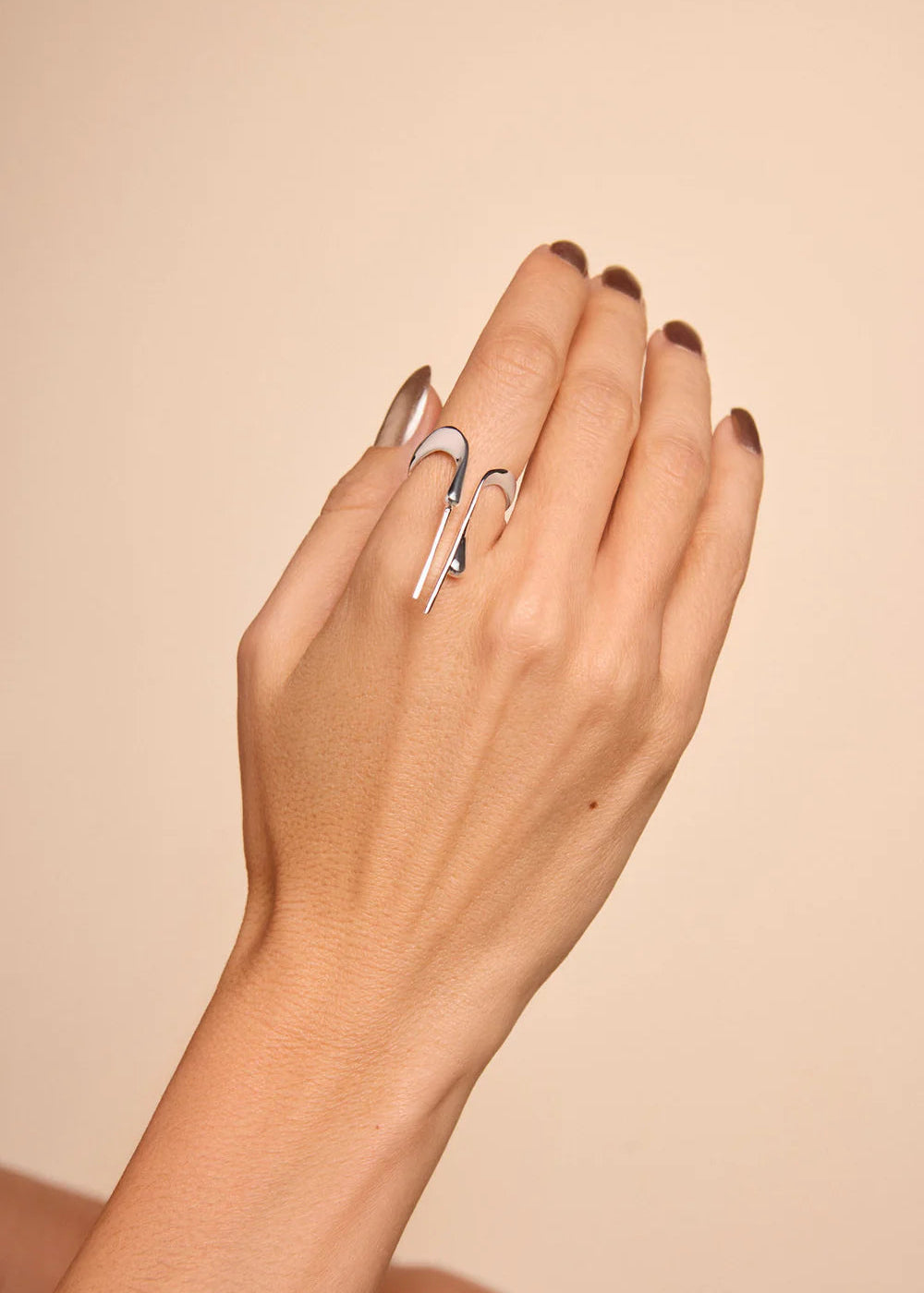 Hand wearing two silver rings on a beige background