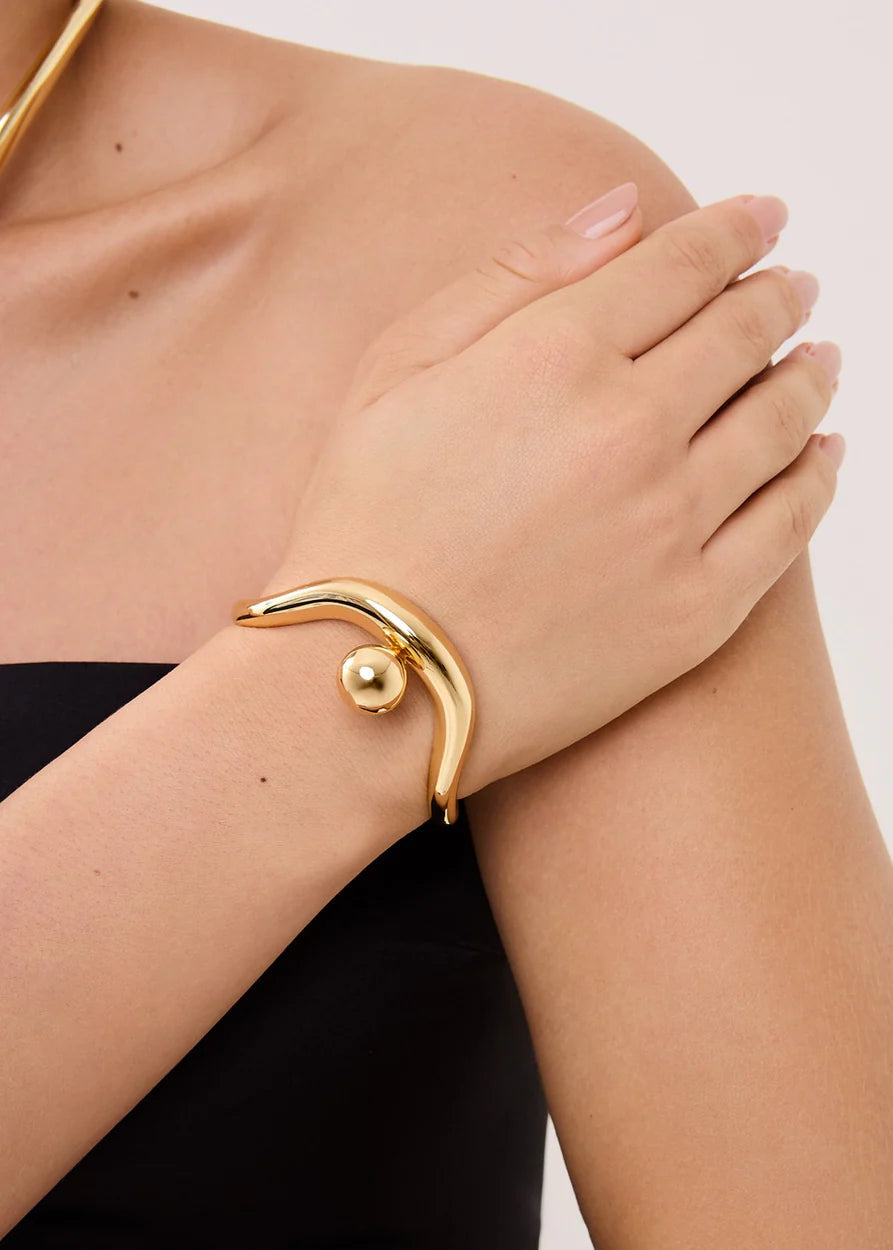 Gold bracelet on a wrist with a plain background
