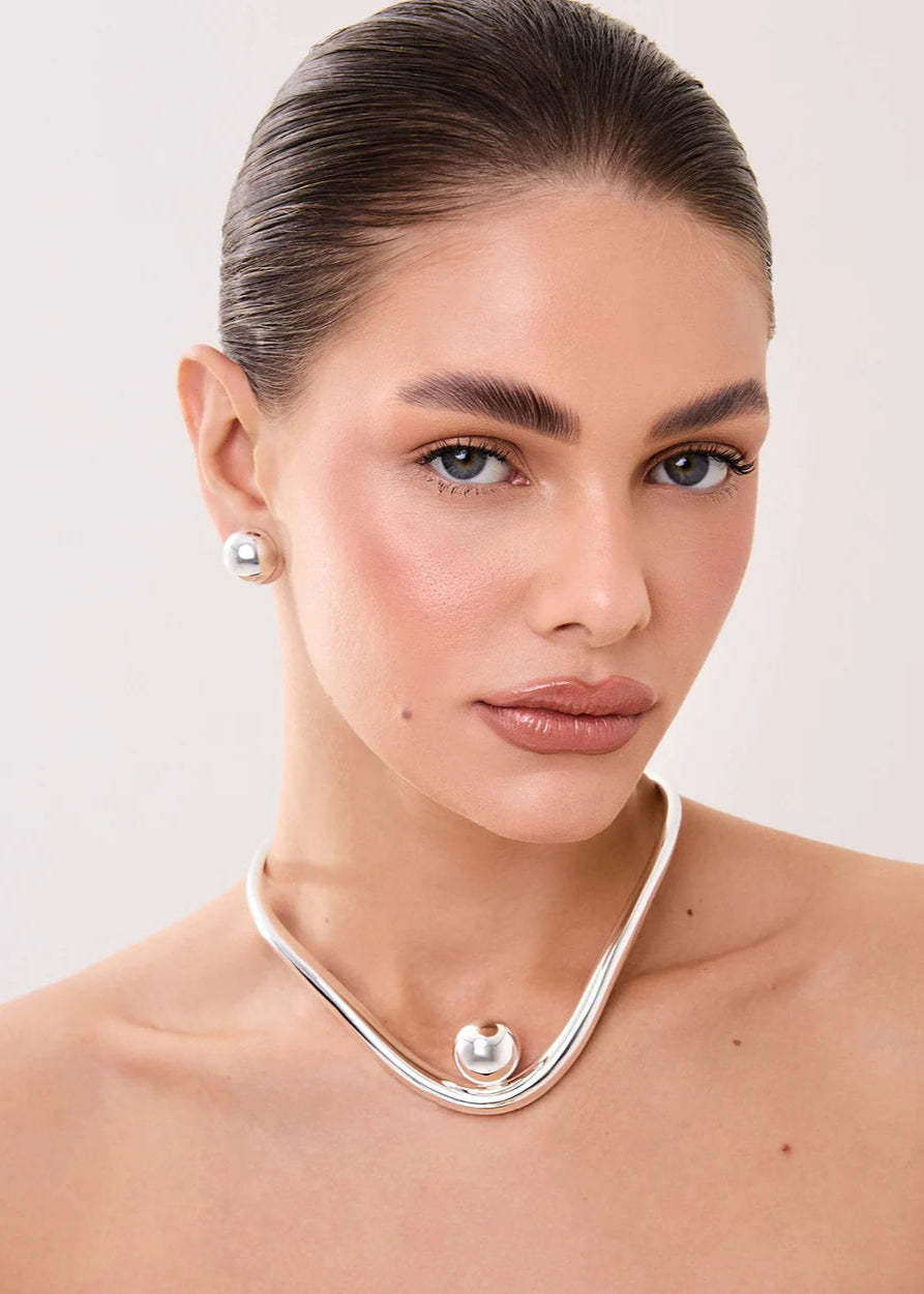 Woman wearing a silver necklace with pearl-like pendants on a plain background