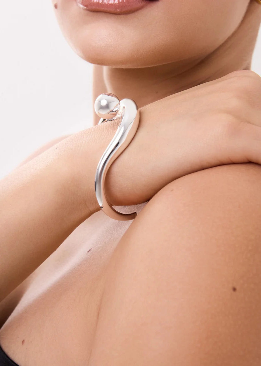 Silver bracelet with a pearl on a person's wrist against a neutral background