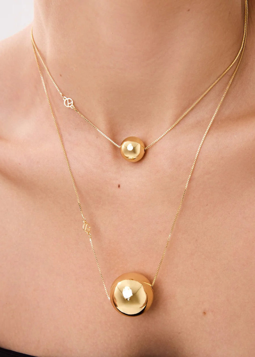 Gold necklace with round pendants on a person's neck against a neutral background