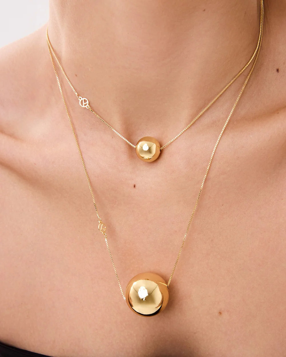 Gold necklace with round pendants on a person's neck against a neutral background
