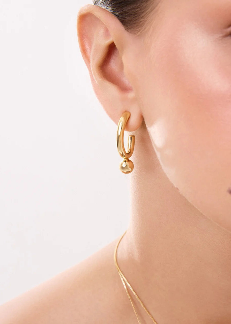 Gold hoop earring worn by a person on a light background