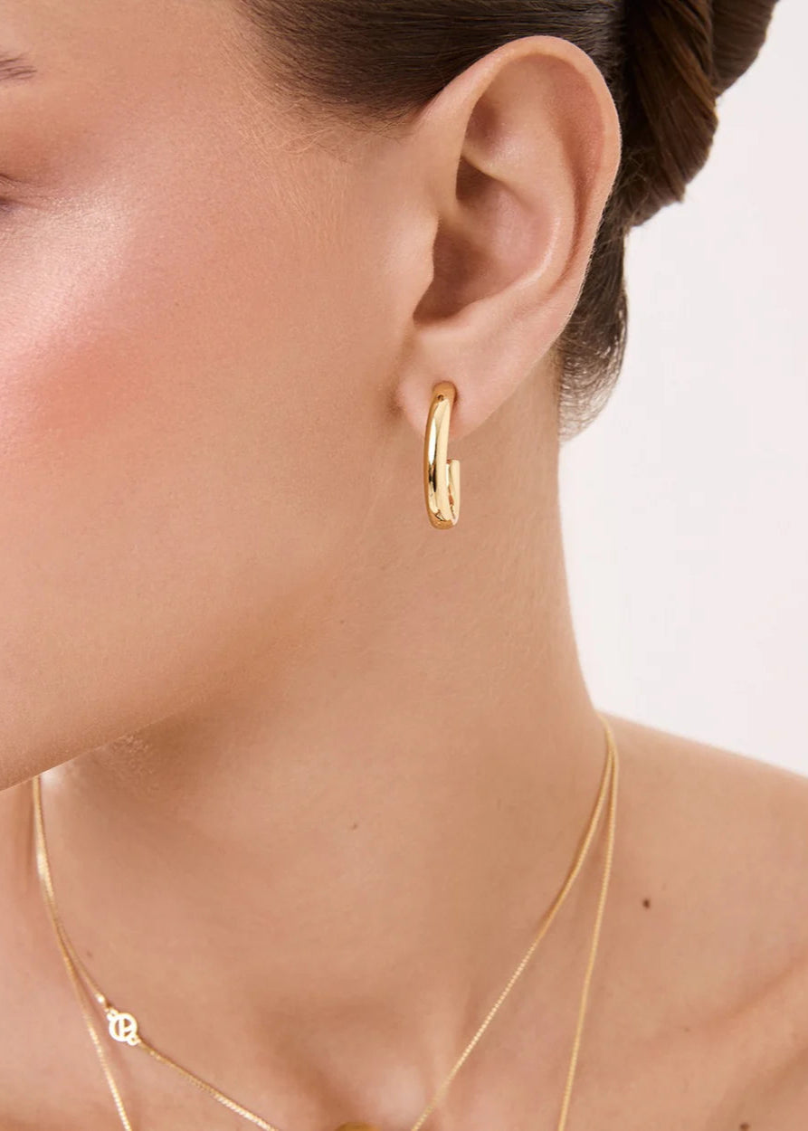 Gold hoop earring worn by a model with a neutral background