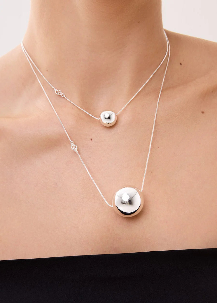 Silver necklace with round pendants on a person's neck against a neutral background