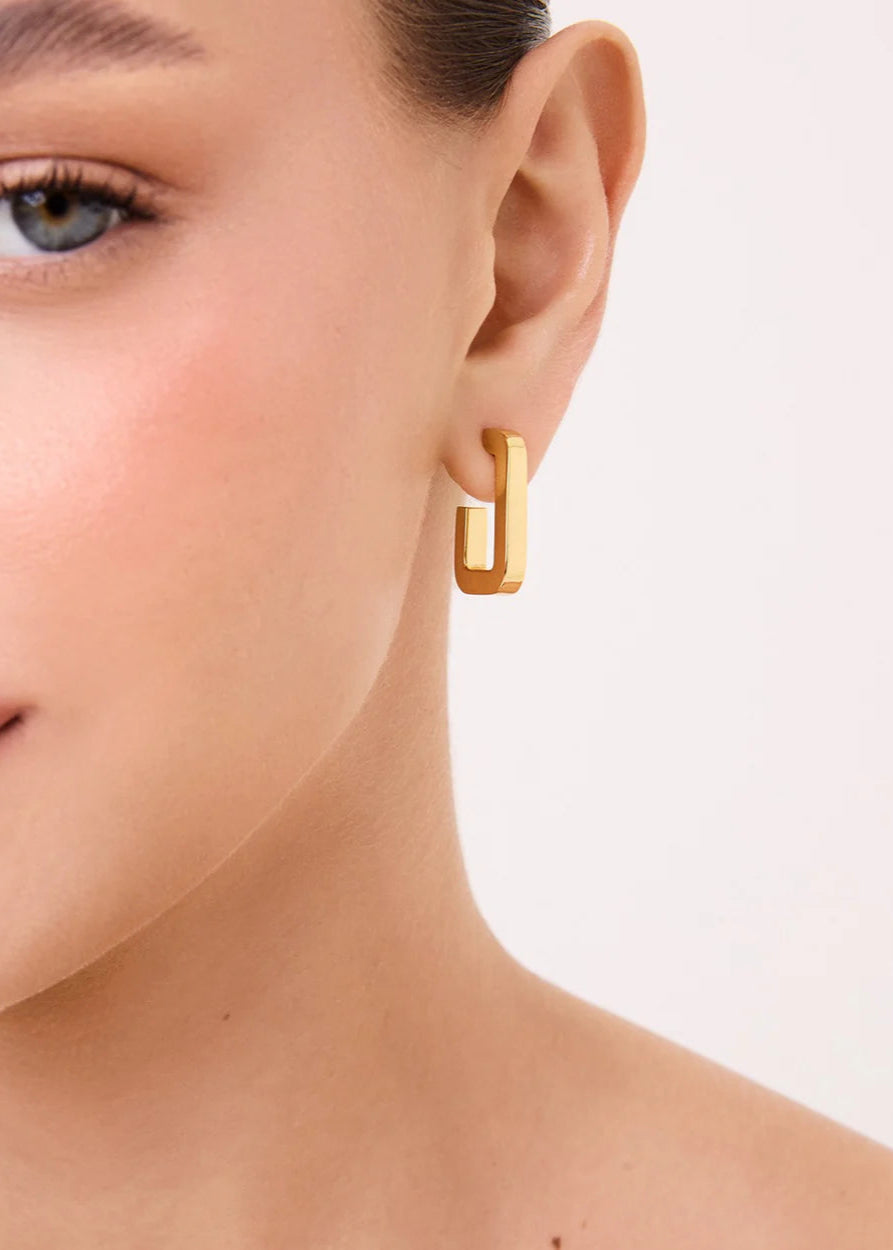 Gold hoop earring worn by a model on a plain background