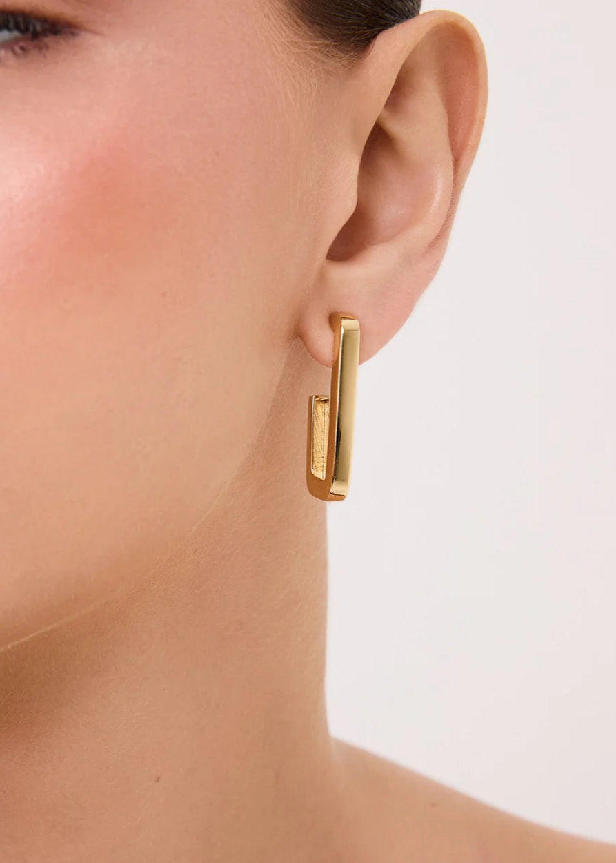 Gold hoop earring worn by a person on a light background