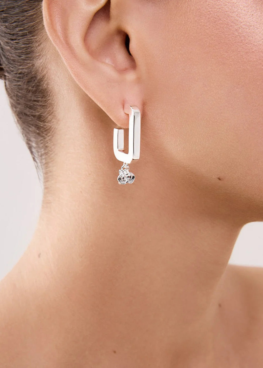 Close-up of a person wearing a silver earring with a heart-shaped pendant on a neutral background