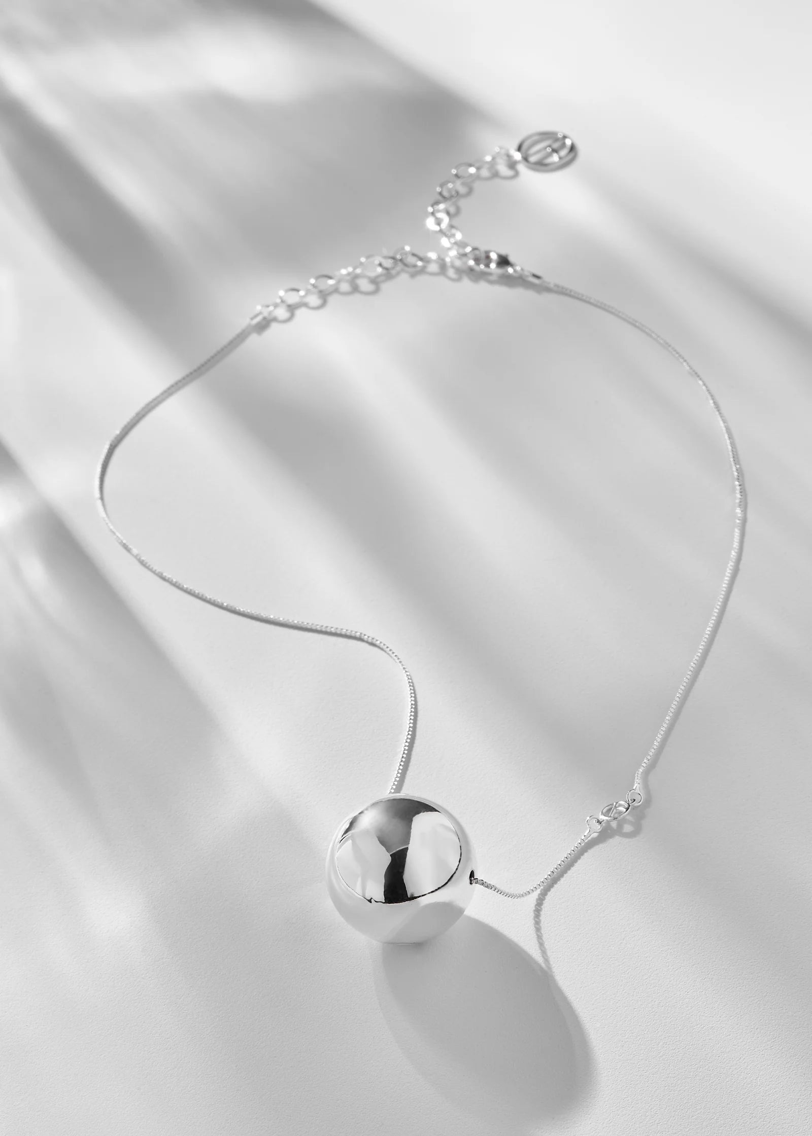 Silver necklace with a spherical pendant on a white satin background