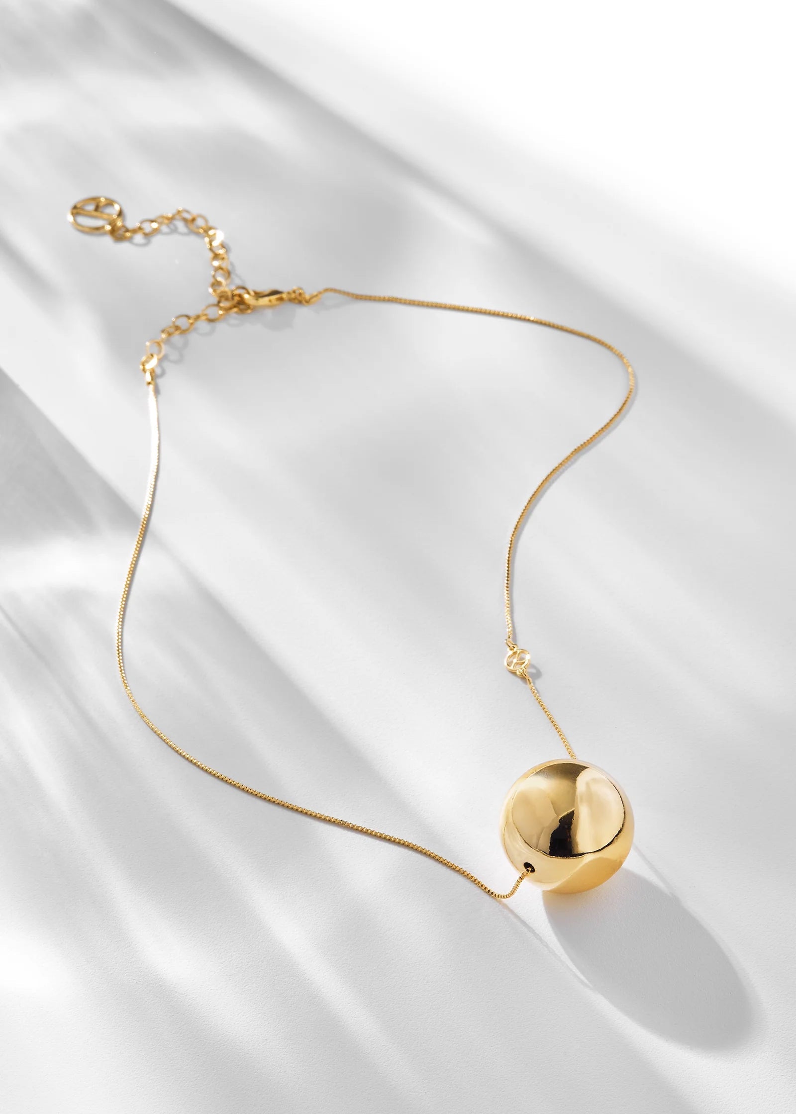 Gold necklace with a spherical pendant on a white fabric background