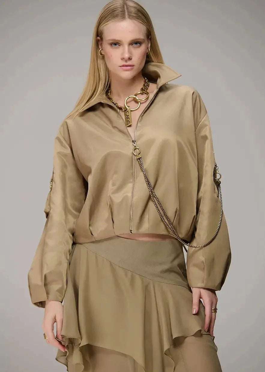 Woman wearing a beige outfit with a chain detail on a gray background