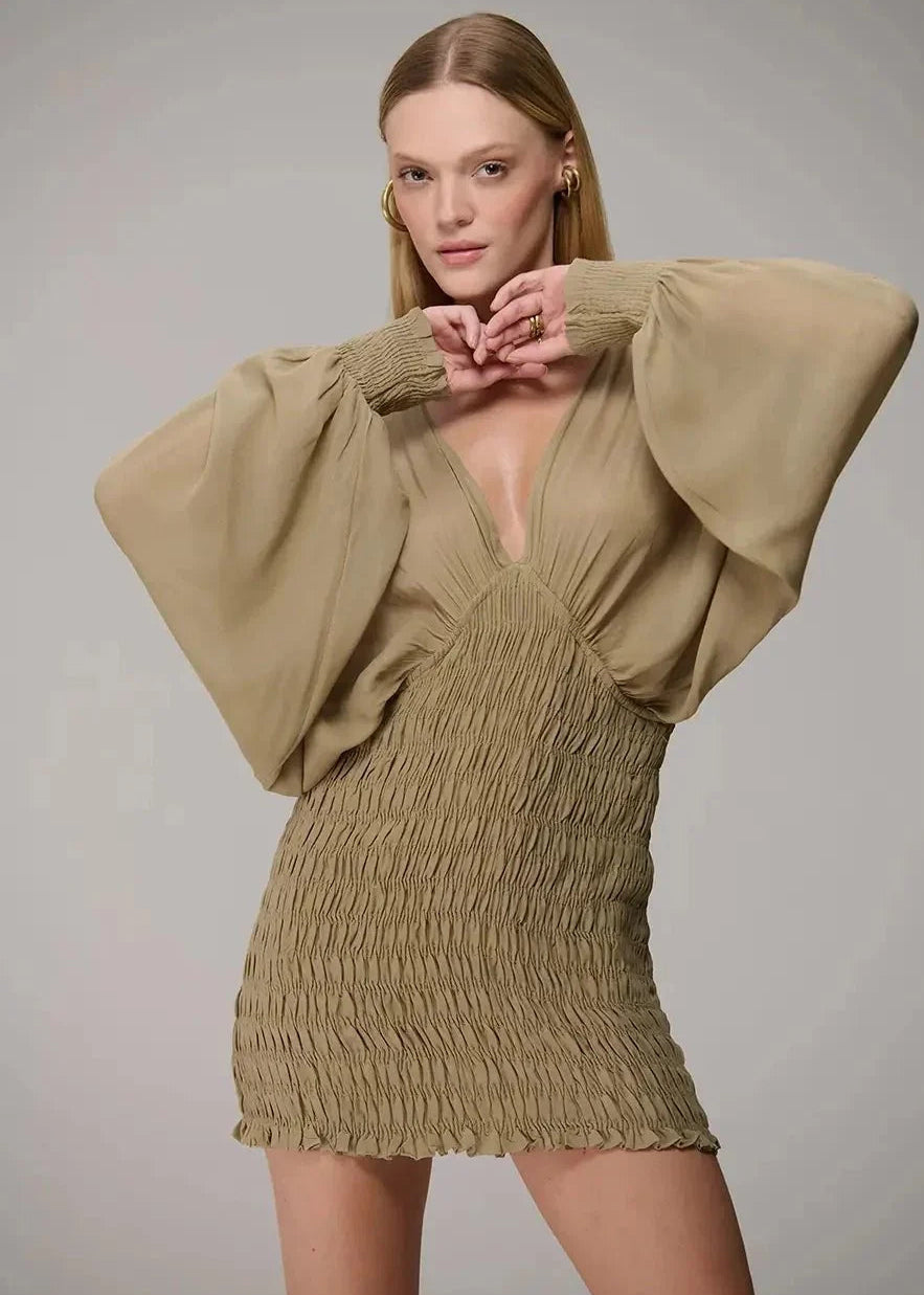 Woman wearing a beige dress with wide sleeves against a plain background