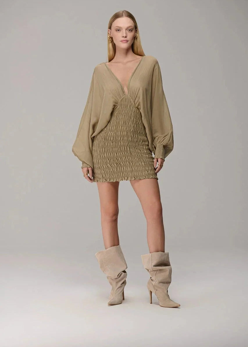 Woman wearing a beige dress and boots on a plain background