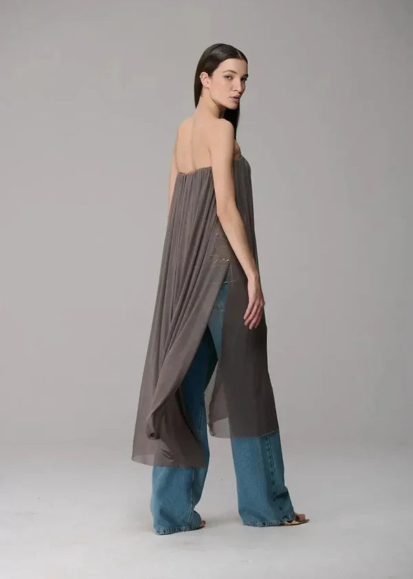 Woman wearing a long, dark army blouse over blue jeans on a plain background