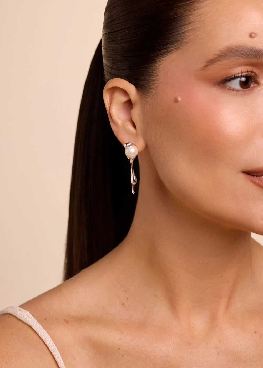 Close-up of a woman wearing a pearl earring against a beige background
