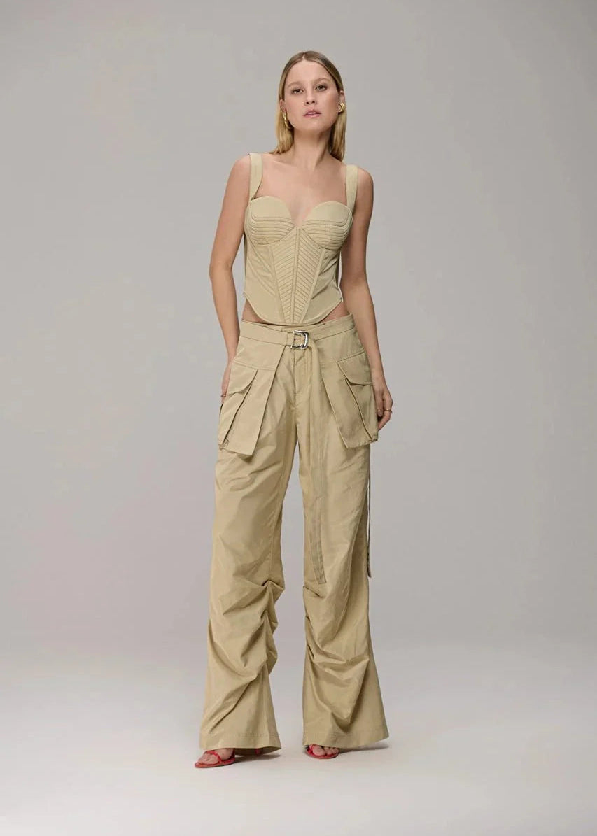 A model wearing a beige two-piece outfit consisting of a structured corset-style camisole top and matching wide-leg cargo pants, standing against a neutral light gray studio background.