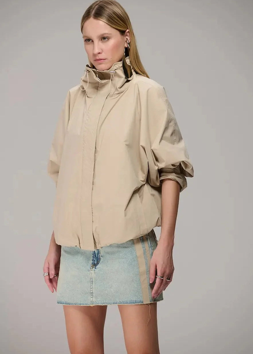 Woman wearing a beige jacket and denim skirt on a gray background
