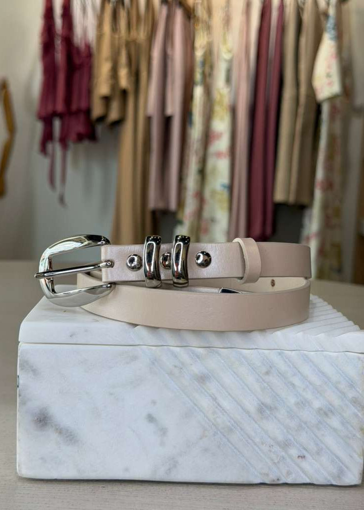Beige belt with silver buckle on a marble box with clothing in the background