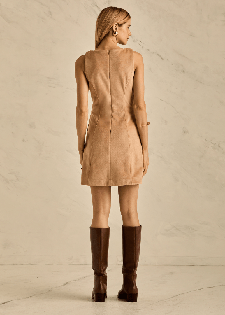 Woman wearing a beige dress and brown knee-high boots against a neutral background