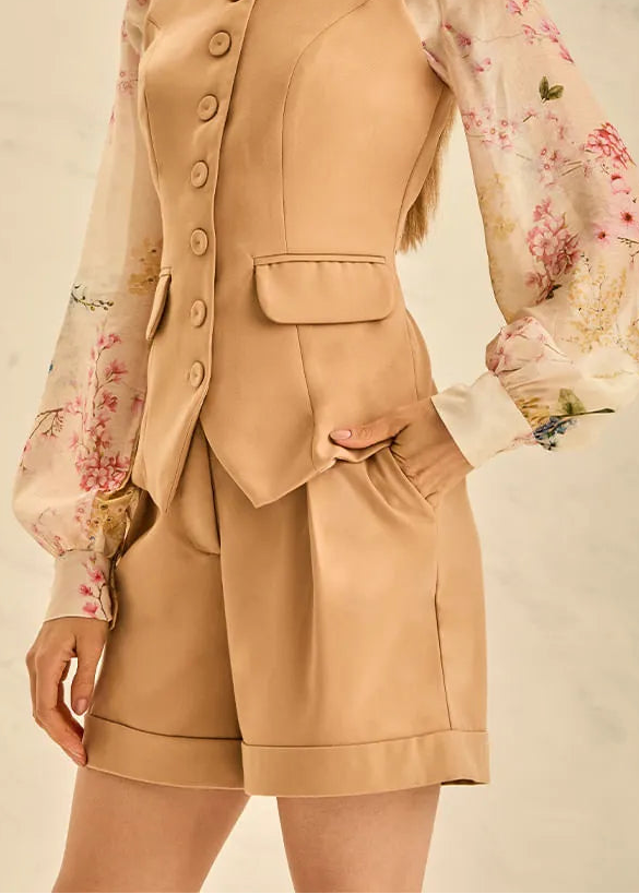 Woman wearing a beige vest and shorts set with a floral blouse against a neutral background