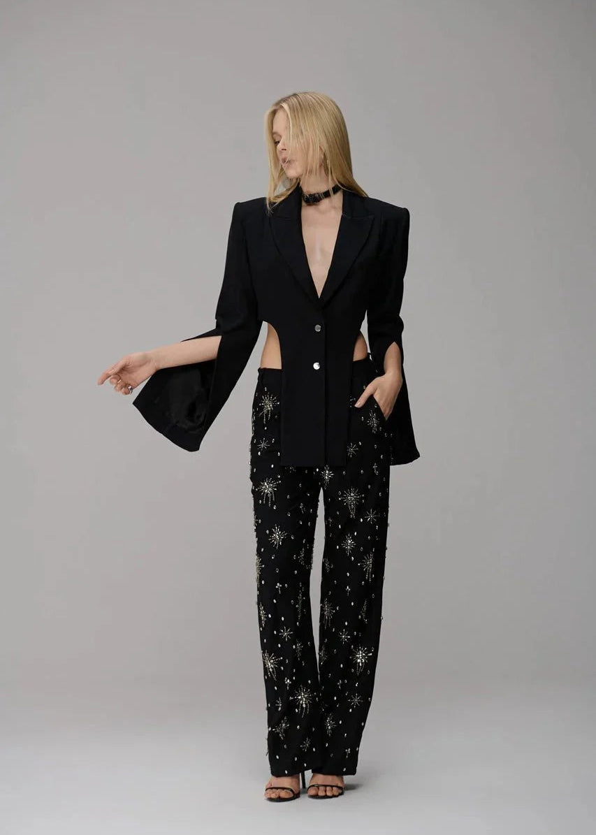 Woman wearing a black suit with star-patterned pants on a gray background