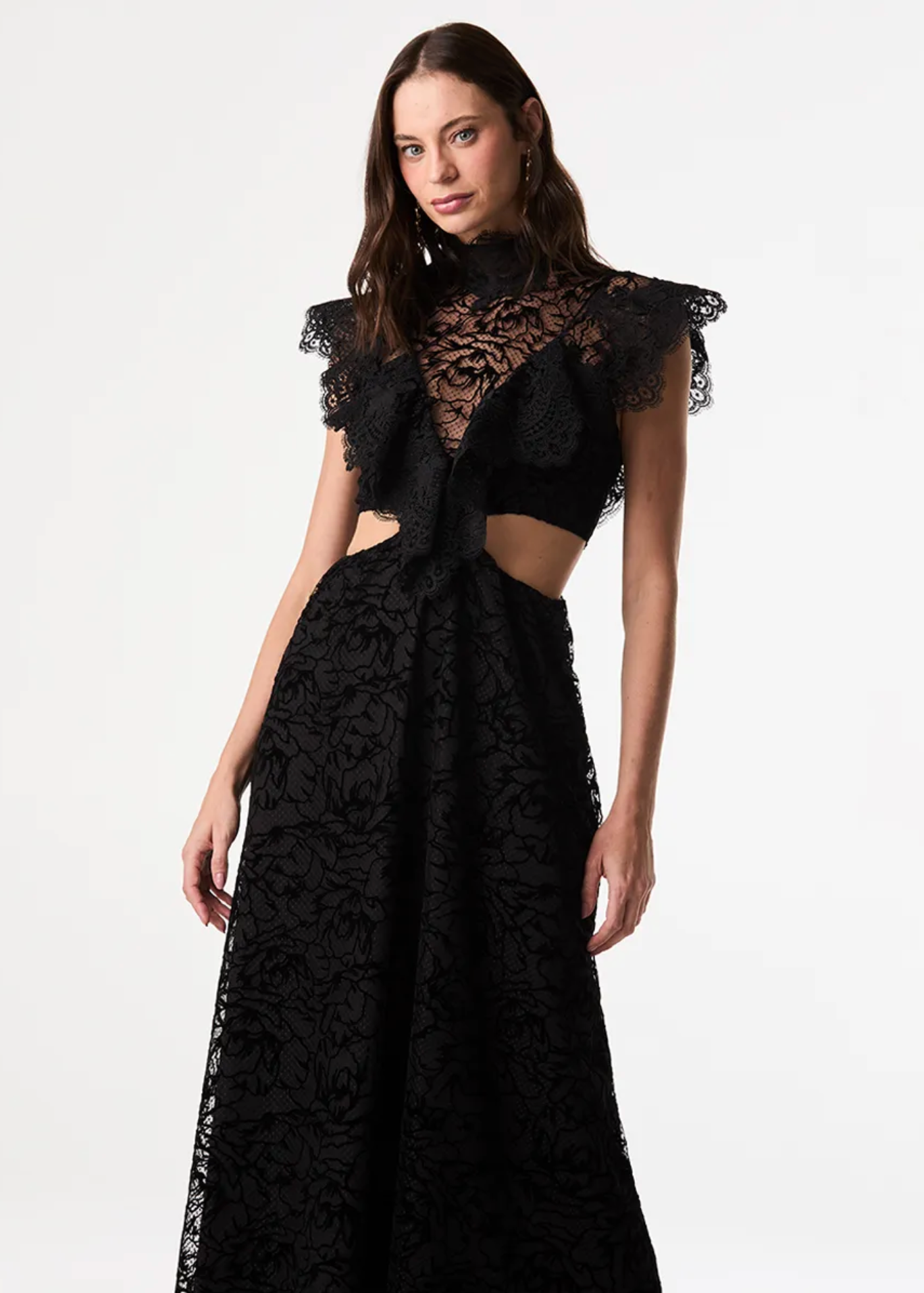 A woman modeling a black lace formal gown with ruffled cap sleeves, a high neckline, side cutouts, and a full skirt against a plain light gray studio background.