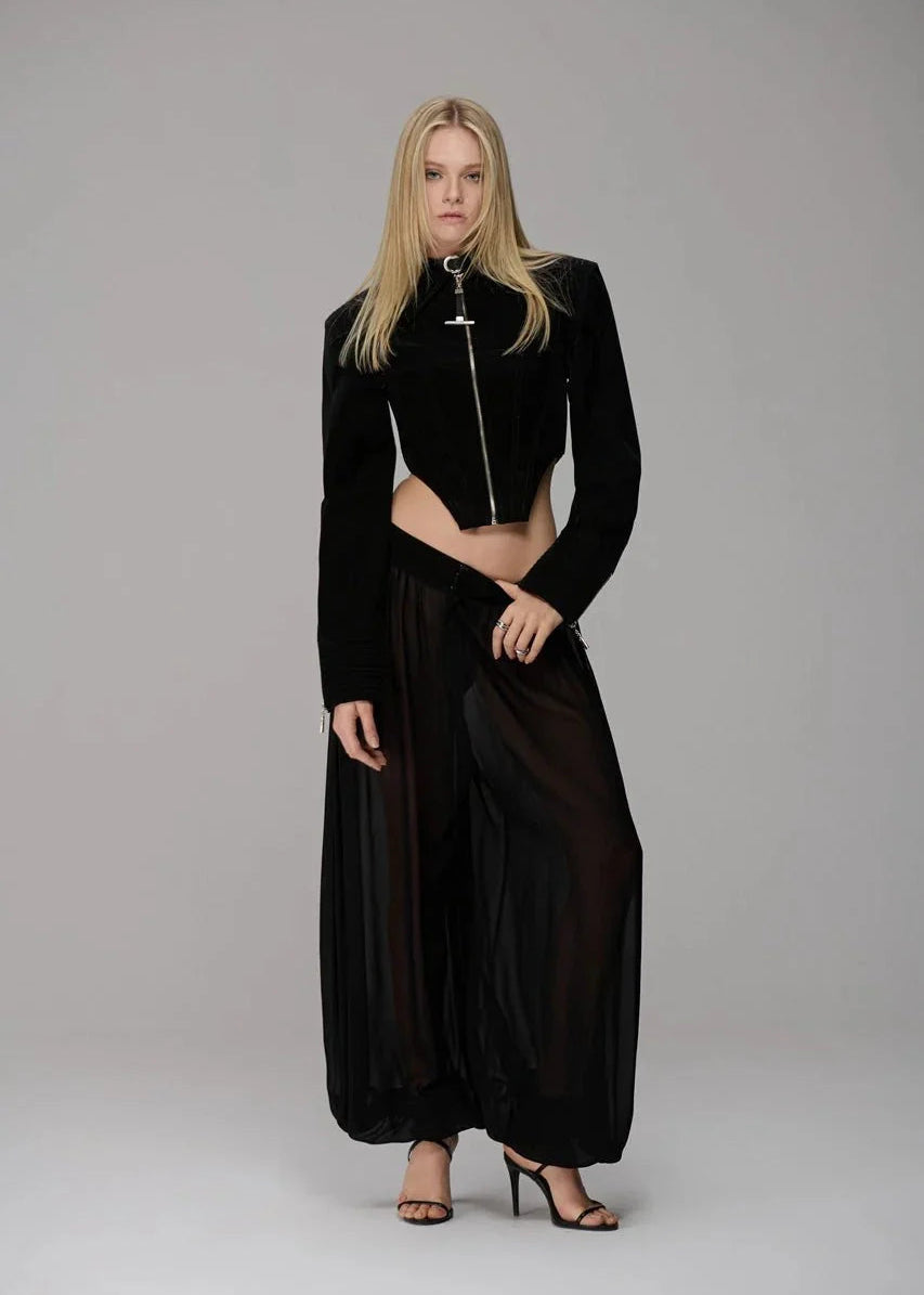 Woman wearing a black outfit with a jacket and long skirt on a gray background