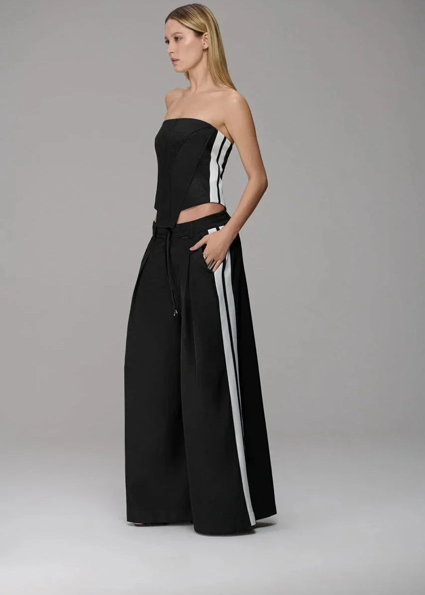Woman wearing a black strapless top and wide-leg pants with white stripes on a gray background
