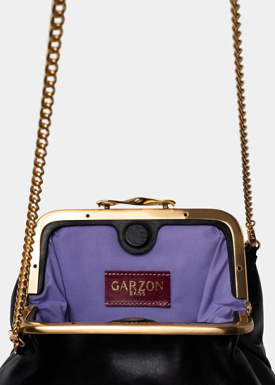 A close-up of a black leather handbag with a gold-tone frame and chain strap, featuring a lavender purple interior lining and a visible GARZON PARIS brand patch.