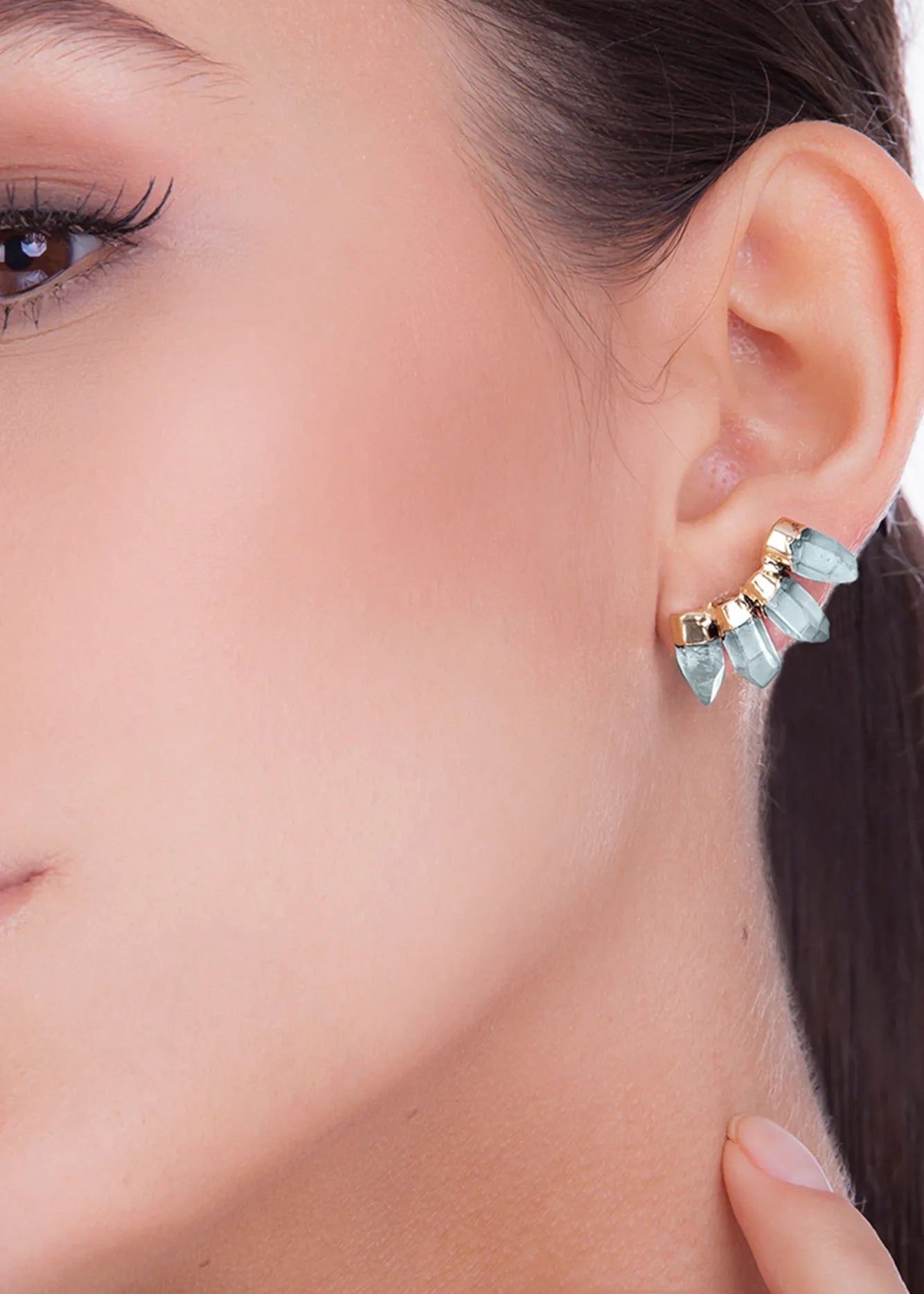 Close-up of a woman wearing a gold earring with blue gemstones.