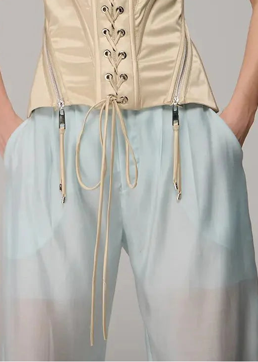 Woman wearing a beige corset and light blue pants against a gray background