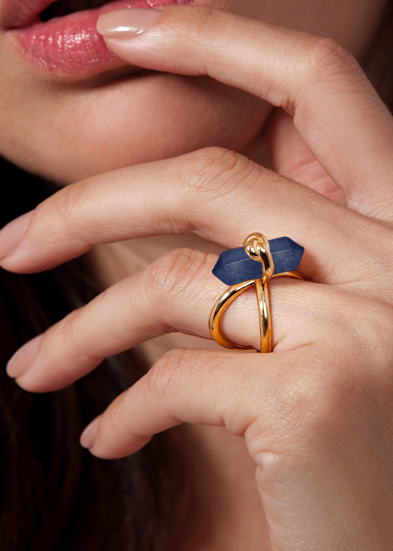 Close-up of a hand wearing a gold ring with a blue stone.