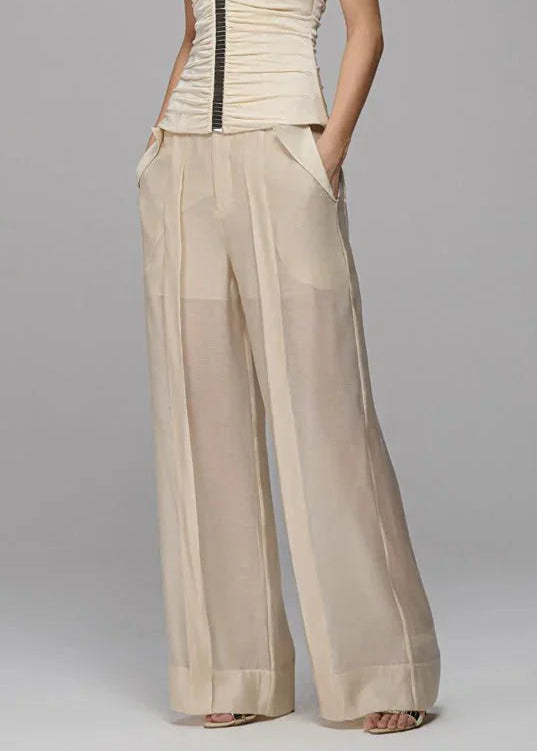Woman wearing a beige strapless top and wide-leg pants on a gray background