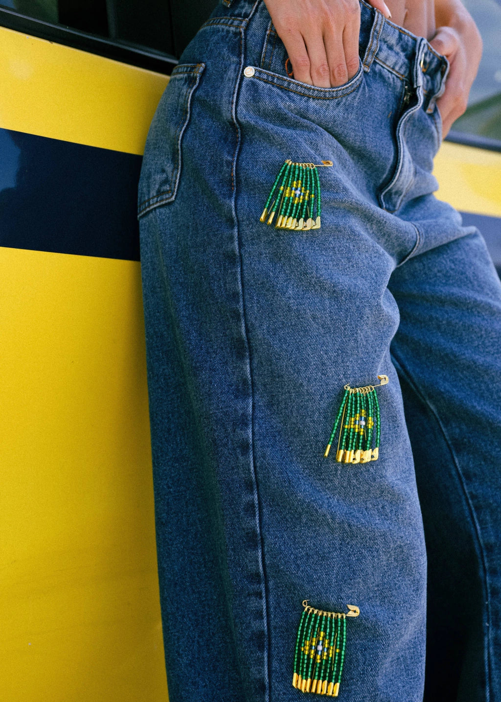 Blue jeans with green beaded patches against a yellow and black background