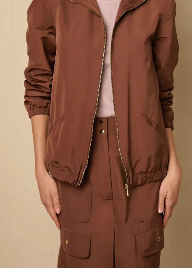 Woman wearing a brown jacket and pants against a beige background