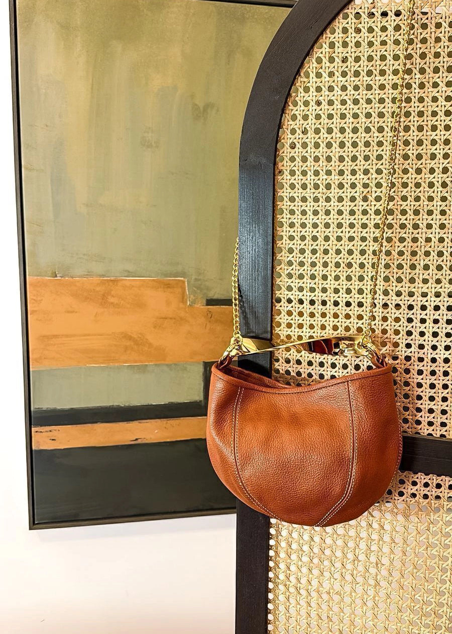 Brown leather handbag hanging on a decorative wall with abstract art in the background