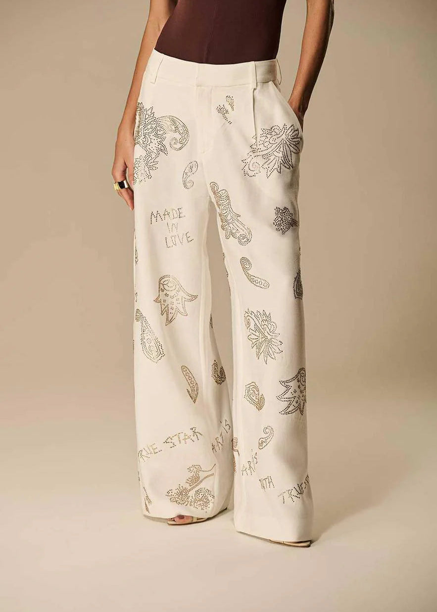 Person wearing white pants with floral patterns on a beige background
