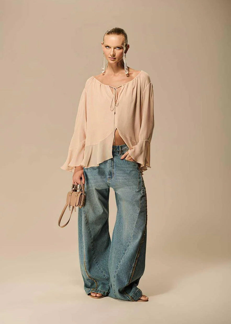 Woman wearing a beige blouse and blue jeans against a beige background